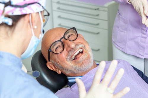 Senior man laughing during a dental checkup while discussing All-on-4 dental implant treatment options with his dentist.