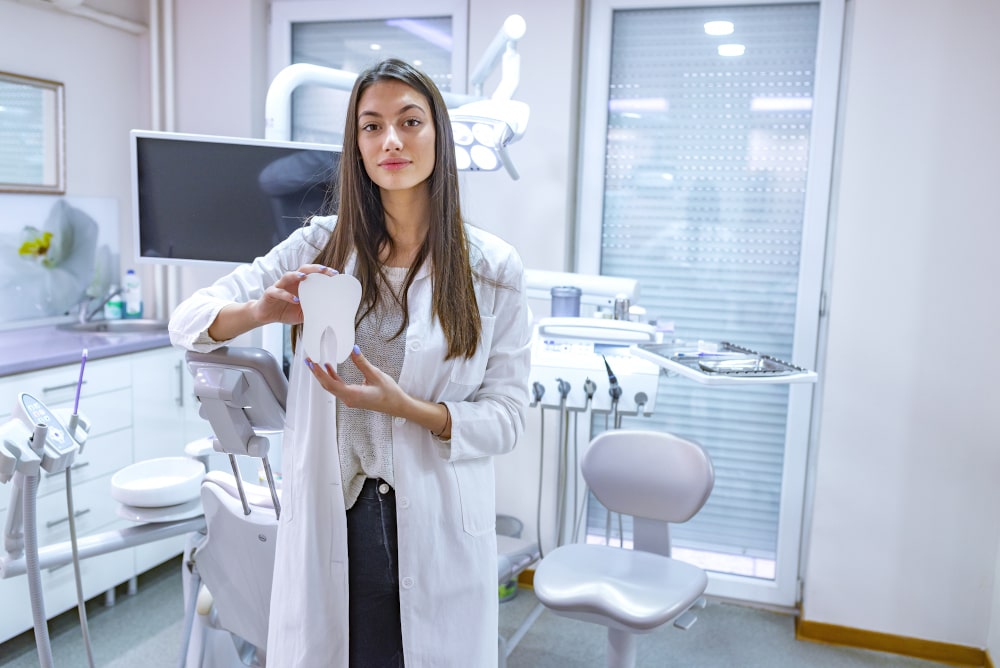 Female dentist holding a tooth model with a crown in a clinic setting